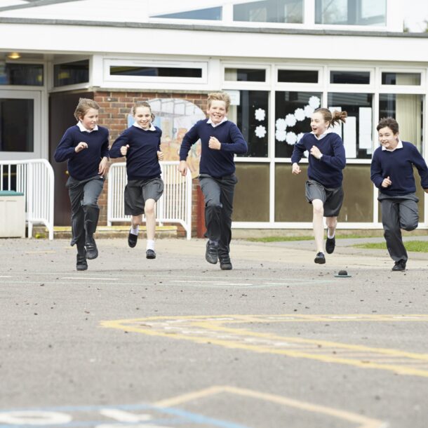 Young people wearing school uniform running across the playground